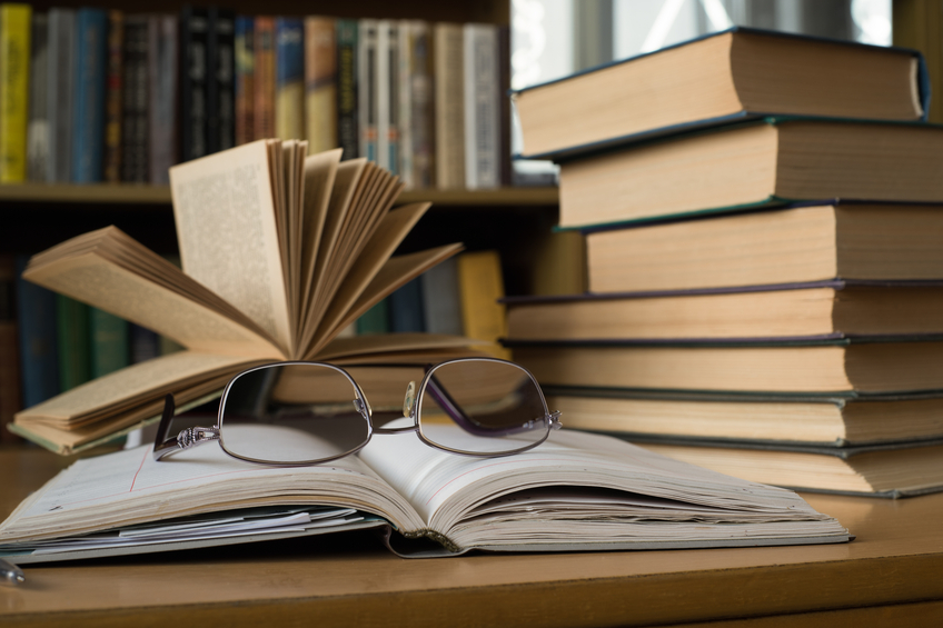 Opened Book with Glasses above and a Stack of Old Books